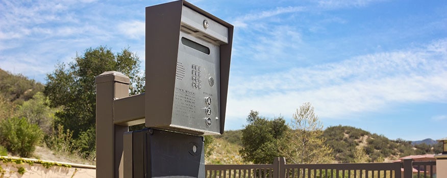 A gate access control system outside a neighborhood surrounded by a fence and overlooking trees and hills