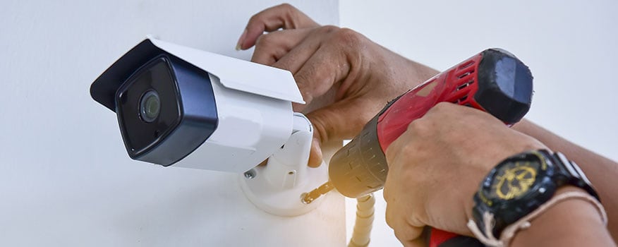 CCTV bullet camera installation into a wall by a person using a red drill