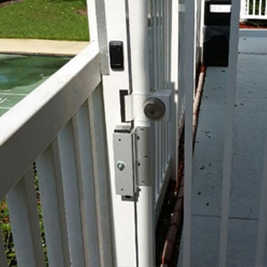 Outdoor view of a white fence and attached locked door that is equipped with a security access control keypad & lock